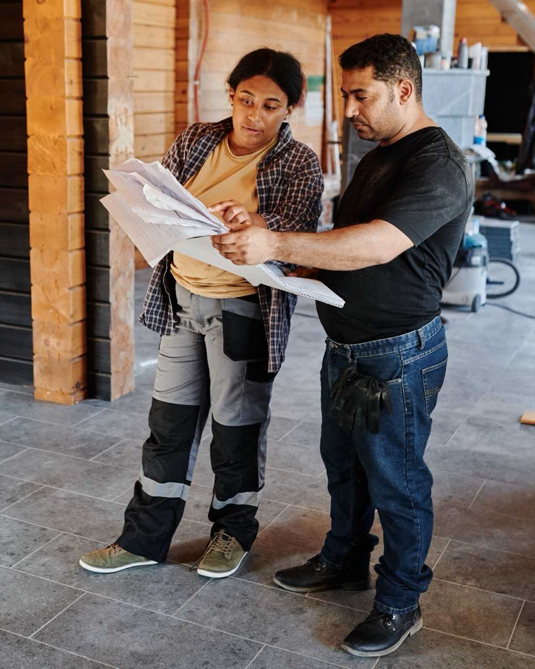 Two builders reading plans together inside a timber house under construction