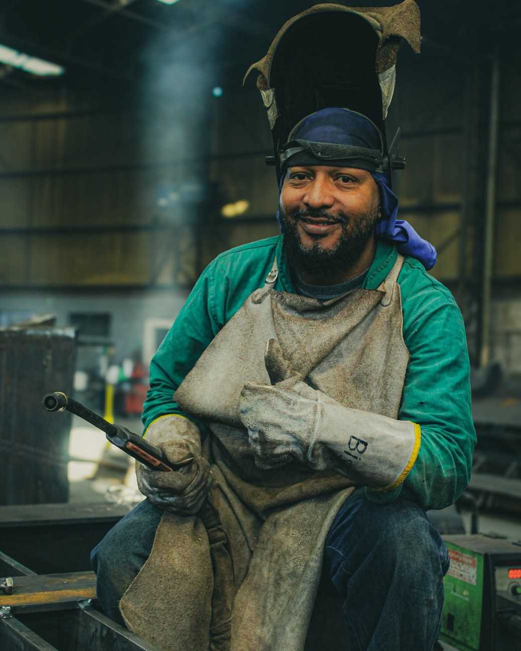 A smiling welder giving a thumbs-up in a metal fabrication shop