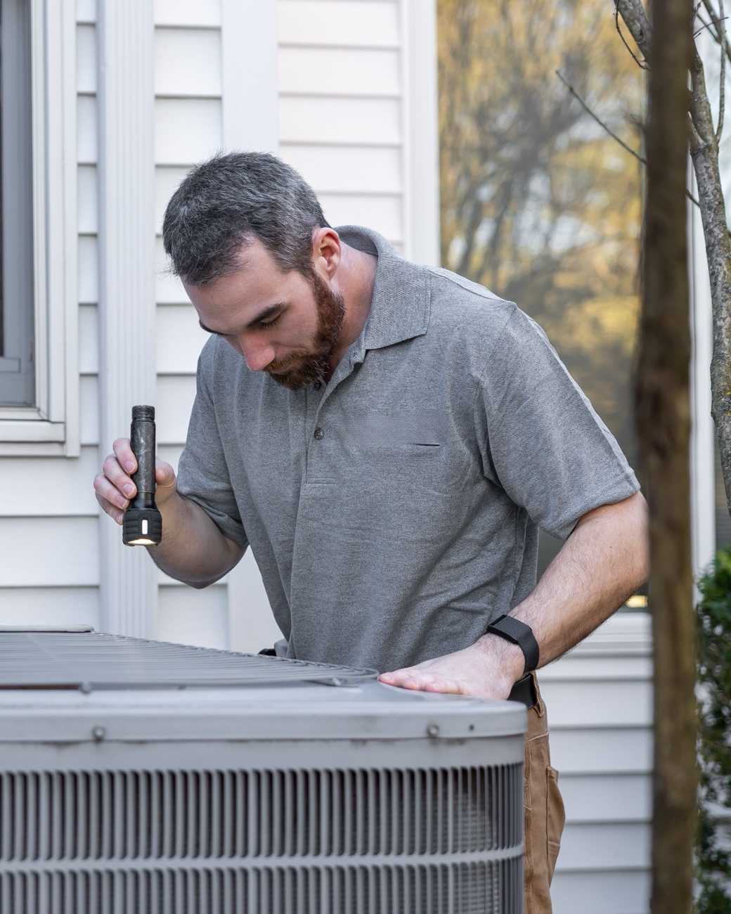 A technician checking an air conditioning unit outside a house