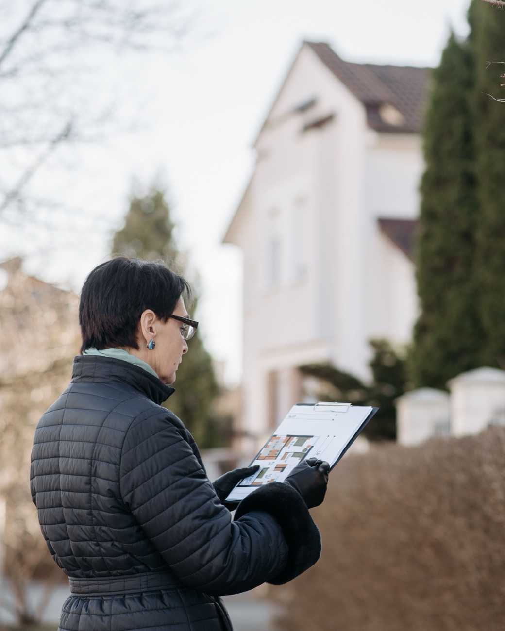 A property manager reviewing papers on a clipboard outside a house