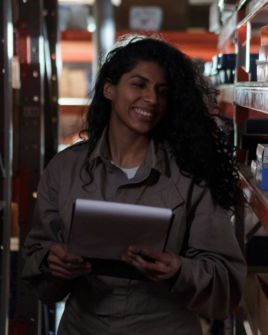A smiling worker holding a clipboard between stockroom shelves