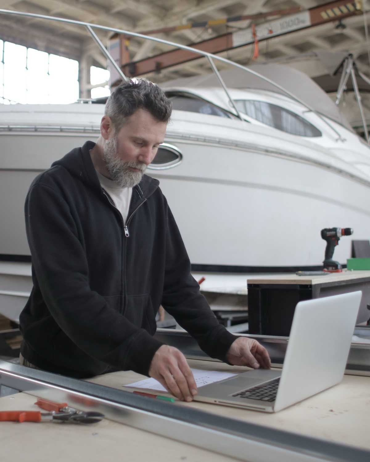 A boat builder checking a laptop at his workbench in a boatyard workshop